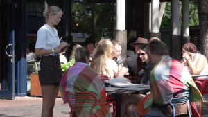 Viesmīle apkalpo apmeklētājus āra terasē Liepājā, kur festivāla laikā cilvēki bauda maltīti un atpūšas.
