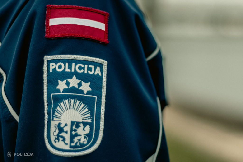 Valsts policijas formas tērps ar policijas emblēmu un Latvijas karogu