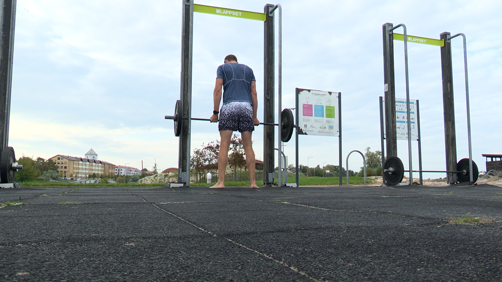 Jaunietis trenējas ar svara stieni āra sporta laukumā