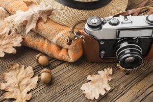 Fotoaparāts, rudens lapas un ozolzīles uz koka galda