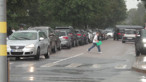Skolēns lietainā laikā šķērso ielu starp automašīnām