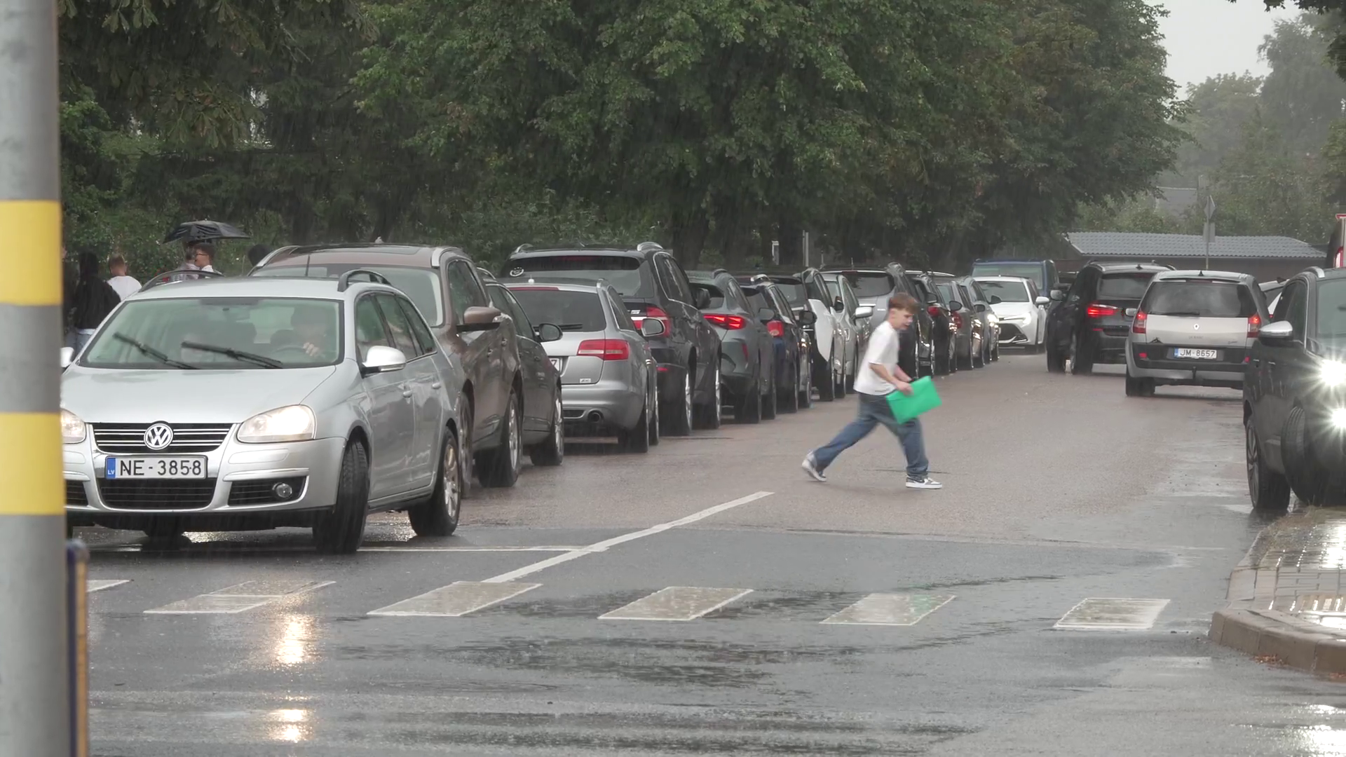 Skolēns lietainā laikā šķērso ielu starp automašīnām