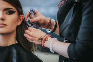 Friziere veido modeles matus, izmantojot matu veidošanas līdzekli. Modelei ir tumši mati un izteiksmīgs grims.
