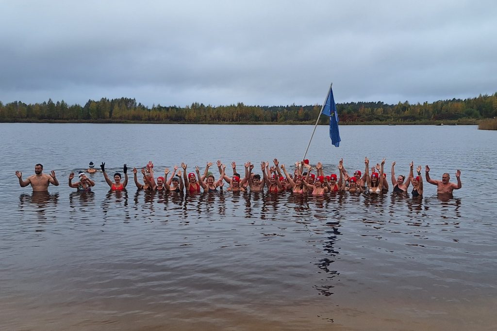Ziemas peldētāju grupa ūdenī ar paceltām rokām.