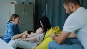 Speciāliste palīdz bērnam vingrot, kamēr vecāki vēro nodarbību
