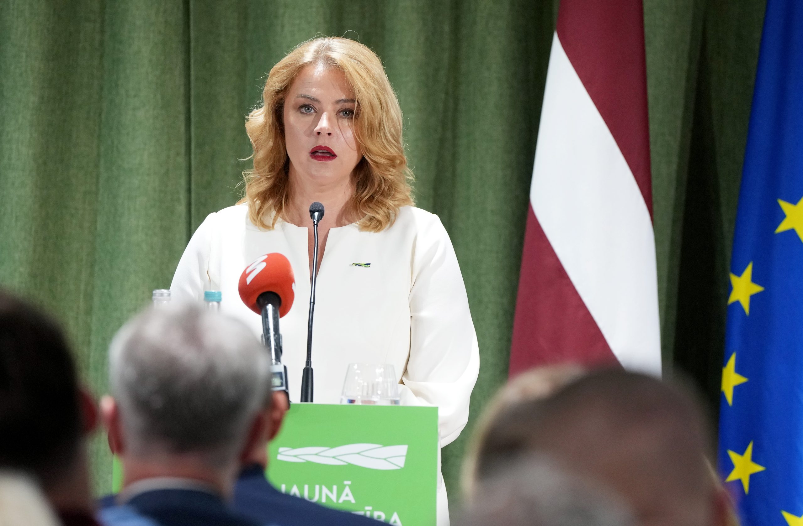 Evika Siliņa uzstājas preses konferencē pie “Jaunās vienotības” tribīnes, fonā Latvijas un Eiropas Savienības karogi.