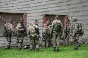 Karavīri militārajā ekipējumā pie ēkas militāro mācību laikā