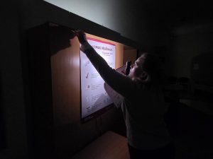 Vēlēšanu iecirkņa darbiniece piestiprina informatīvo plakātu 15. Saeimas vēlēšanu laikā