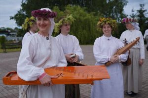 Sievietes tautastērpos un ziedu vainagos ar tradicionālajiem mūzikas instrumentiem.