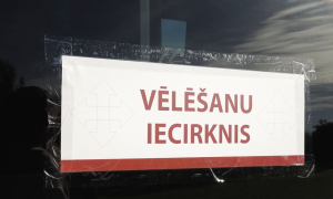 Alt text: Norāde “Vēlēšanu iecirknis” pie ieejas balsošanas vietā