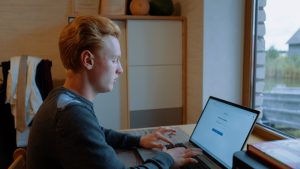 Jaunais uzņēmējs Emīls Nils Gaišprātis sēž pie galda un strādā ar portatīvo datoru.