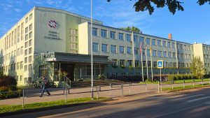 Jelgavas Spīdolas Valsts ģimnāzijas ēka ar skolas galveno ieeju, karogiem un labiekārtotu apkārtni.