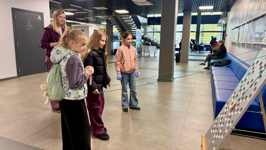 Trīs meitenes piedalās sportiskā uzdevumā Jēkabpils Sporta hallē.