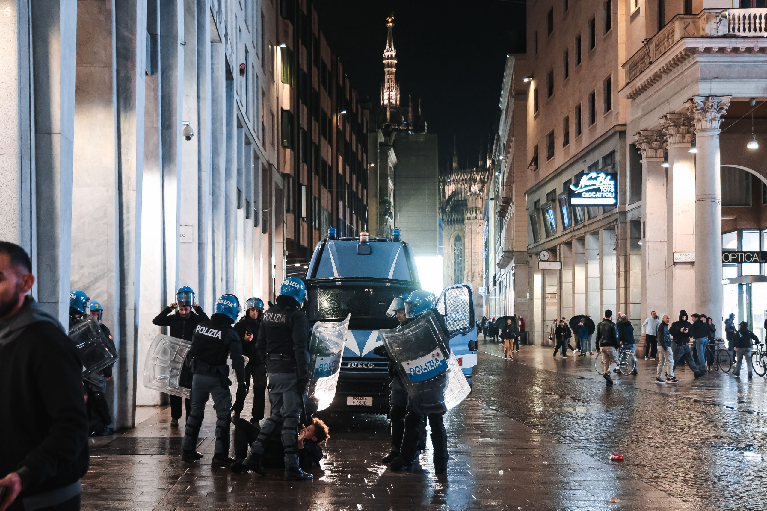Itālijas policisti aiztur cilvēku pie policijas transportlīdzekļa Milānas centrā.