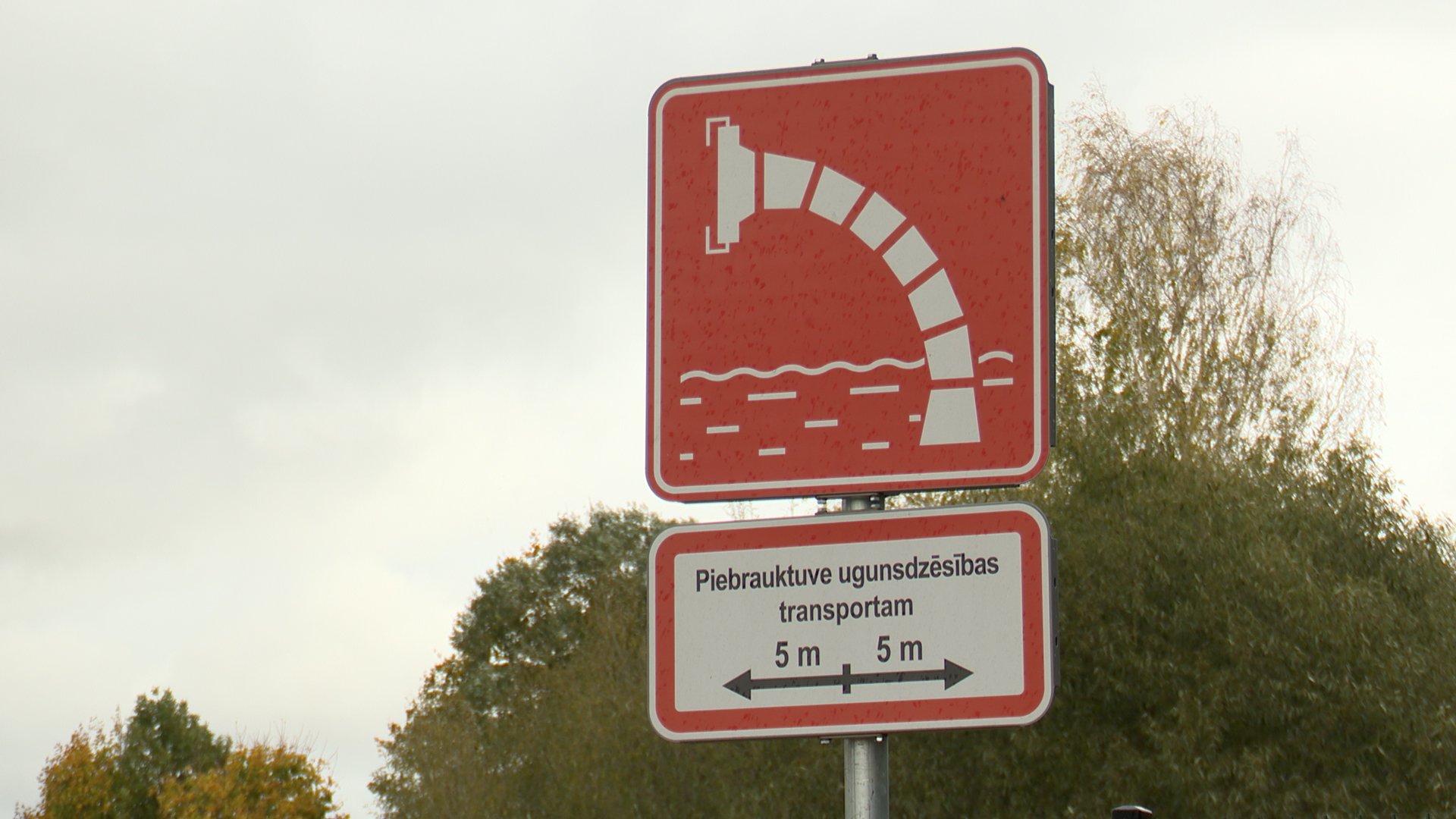 Sarkana ugunsdzēsības ūdens ņemšanas vietas zīme ar norādi par piebrauktuvi ugunsdzēsības transportam.