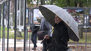 Sieviete ar lietussargu aplūko brīvdabas fotogrāfiju izstādi Liepājā.